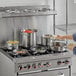 A woman cooking with Vollrath stainless steel pans on a stove.