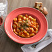 A Tuxton Cinnebar China bowl filled with pasta on a table with a glass of wine.