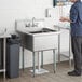 A man standing in a kitchen with a Regency stainless steel 1 compartment sink.