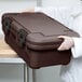 A woman using a Cambro dark brown food pan carrier on a counter.