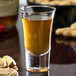 A Libbey shot glass filled with brown liquid on a table.