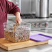 A person in a chef uniform pouring a mixture of beans into a Vigor food storage container.