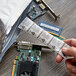 A hand holding a piece of paper with a computer chip next to a Multisorb NatraSorb silica packet.