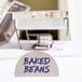 An American Metalcraft stainless steel menu card sign with blue text that says "Baked Beans" on a hotel buffet table.