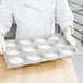 A person in a white coat holding a Chicago Metallic mini cake and jumbo muffin pan filled with cupcakes.