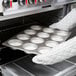 A gloved hand holding a Chicago Metallic mini cake/jumbo muffin pan filled with baked muffins.