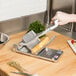 A person using a Nemco Easy Cheeser to cut cheese on a cutting board.