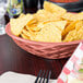 A paprika round weave basket filled with chips on a table.