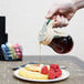 A person using a Tablecraft glass syrup dispenser to pour syrup on a plate of food.