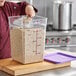 A woman in a chef's uniform pouring oats into a Vigor clear food storage container.