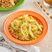 An Acopa Valencia orange stoneware plate with noodles, vegetables, and meat.