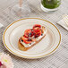 A WNA Comet ivory plastic plate with gold accent bands holding food on a table.