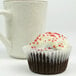 A cupcake with white frosting and red sprinkles in a white fluted paper wrapper.