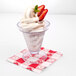 A clear plastic cup of ice cream with strawberries on top.