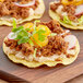 Three tacos filled with meat and vegetables on a wooden cutting board.