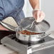 A person cooking food in a stainless steel saute pan on a stove.