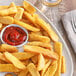 A yellow container of Regal Seasoned Salt on a white background next to a plate of french fries with ketchup.