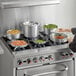 A woman cooking with a Choice aluminum cookware set on a stove.