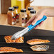 A person using Choice blue stainless steel scalloped tongs to grill fish.