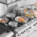 A woman cooking food in Vigor stainless steel pans on a stove.