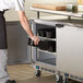 A person in a blue shirt and gloves putting a black tray into a Beverage-Air undercounter freezer.