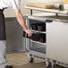 A person using a glove to put a black tray into a Beverage-Air undercounter freezer.