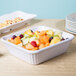 A bowl of fruit in a white rectangular casserole dish with plates of food on it.