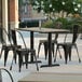 A Lancaster Table & Seating rectangular dining height table with textured metal base plates on an outdoor patio with chairs.