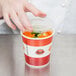 A hand using a Choice paper soup and hot food container to hold food.