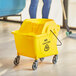 A woman using a yellow Lavex mop bucket to clean a wood floor.