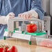 A person in gloves using a Garde 7/32" tomato slicer blade to cut a tomato on a cutting board.