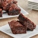 A plate of brownies with a fork and knife on a white table.