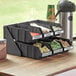 A black plastic Choice 2-tier tray with bins and labels on a counter.