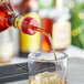 A person using a Choice Red Free Flow Whiskey Pourer to pour a drink into a glass on a table.