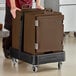 A man pushing a brown CaterGator front loading food pan carrier with wheels.