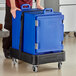 A man pushing a large blue CaterGator food pan carrier on a black dolly with a strap.