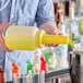 A person pouring liquid from a yellow Choice pour bottle into a cup.