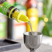 A neon yellow Choice liquor pourer on a bottle of yellow liquid being poured into a glass.