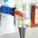 A red liquor pourer pouring liquid into a metal cup.