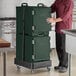A man in a chef's uniform holding a green CaterGator pan carrier box.