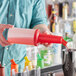 A person pouring liquid from a red Choice pour bottle into a cup.
