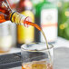 A person using a Choice red free flow whiskey pourer to pour a drink into a glass.