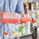 A person using a Choice pour bottle with a red flip top to pour red liquid into a cup.