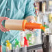 A person pouring liquid from a plastic container with an orange cap.