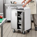 A man standing in a kitchen with a Regency stainless steel utility cart full of plates.