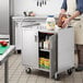 A man using a Regency stainless steel utility cart with enclosed shelves to transport food.