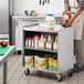 A person standing next to a Regency stainless steel utility cart with jars of food on it.