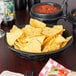 A charcoal round weave basket filled with tortilla chips and a bowl of salsa on a table.