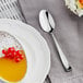 An Acopa Monte Bianco stainless steel teaspoon on a table next to a plate with dessert.