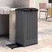 A grey Suncast Trash Hideaway with a lid on a stone patio.